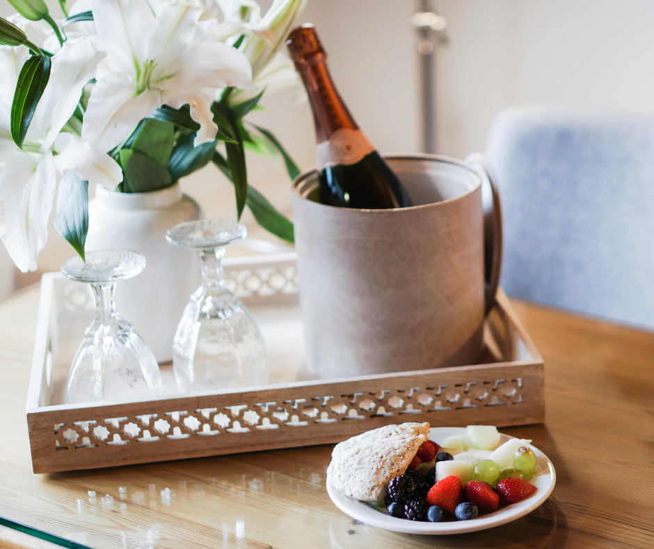 A vase of flowers, a bucket of champagne and glasses, and a plate of food on a table.