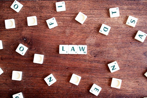 Scrabble tiles spread across a wooden surface, with three put together to create the word 'Law'