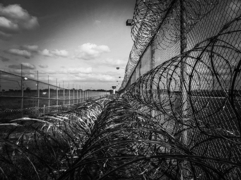 A barbed wire prison fence in black and white.