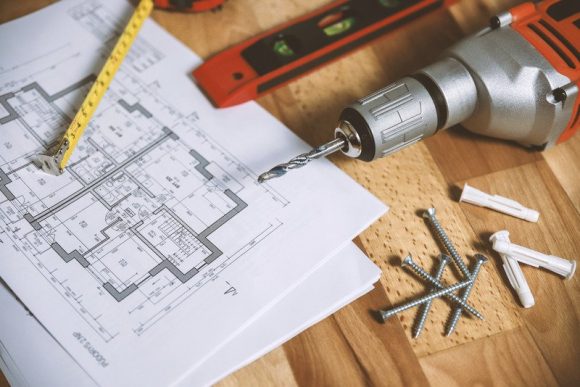 A floor plan on on a table with a tape measure, level, drill and screws.