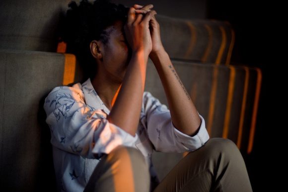 A woman showing signs of anxiety and stress by sitting with her hands covering her face.