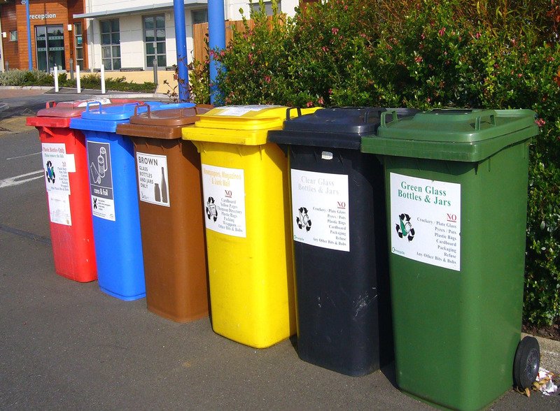 A row of multiple colours of recycling bins.