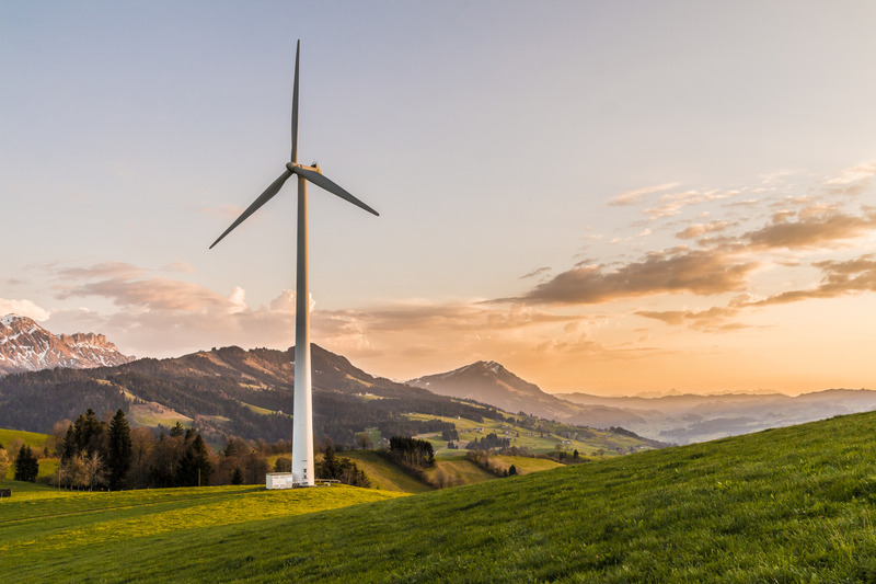 A wind turbine in a field surrounded by cliffs and trees.