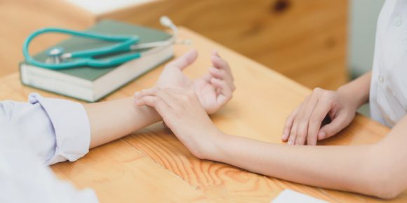 Cropped shot of young female doctor checking her patient pulse whith her hand in clinic room