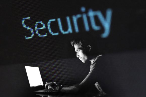 A man on a laptop in black and white with the word 'Security' over his head in blue.