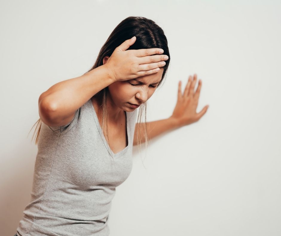 Woman with a headache holding her forehead with one hand and propping herself against a wall with the other