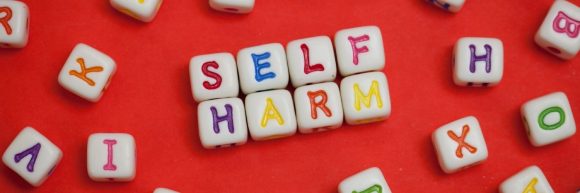 Letter dice spelling out 'self harm'