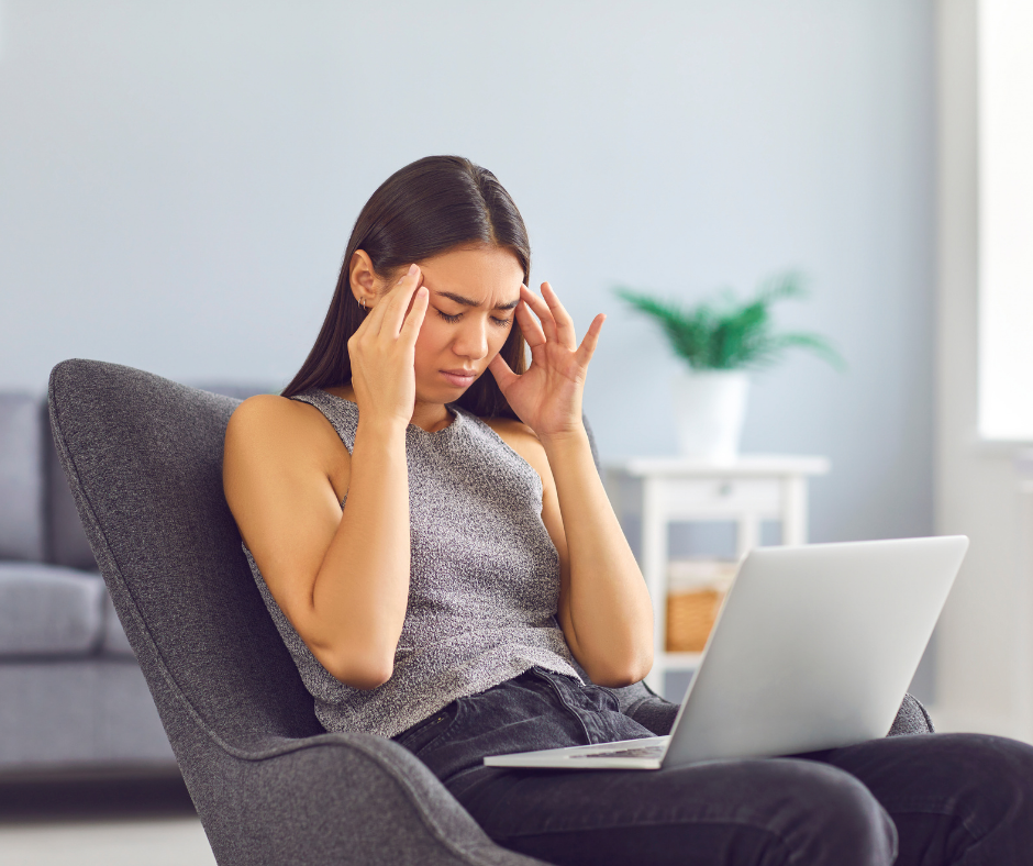 Woman sat in a chair with laptop holding her head in pain