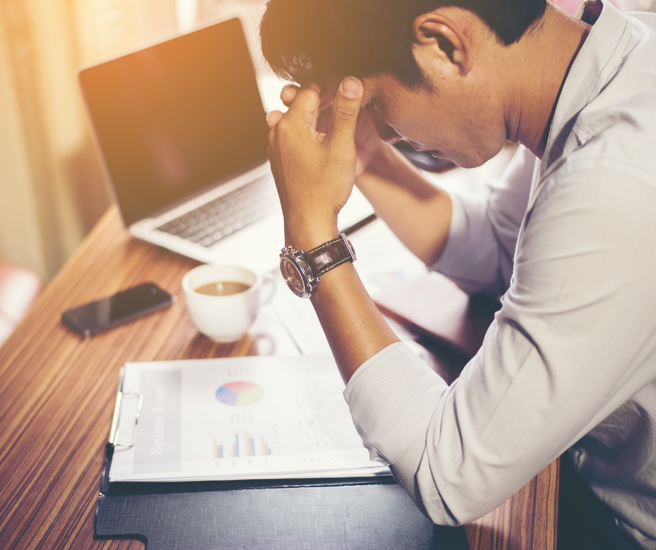 Man sitting at a work desk, holding his head looking stressed